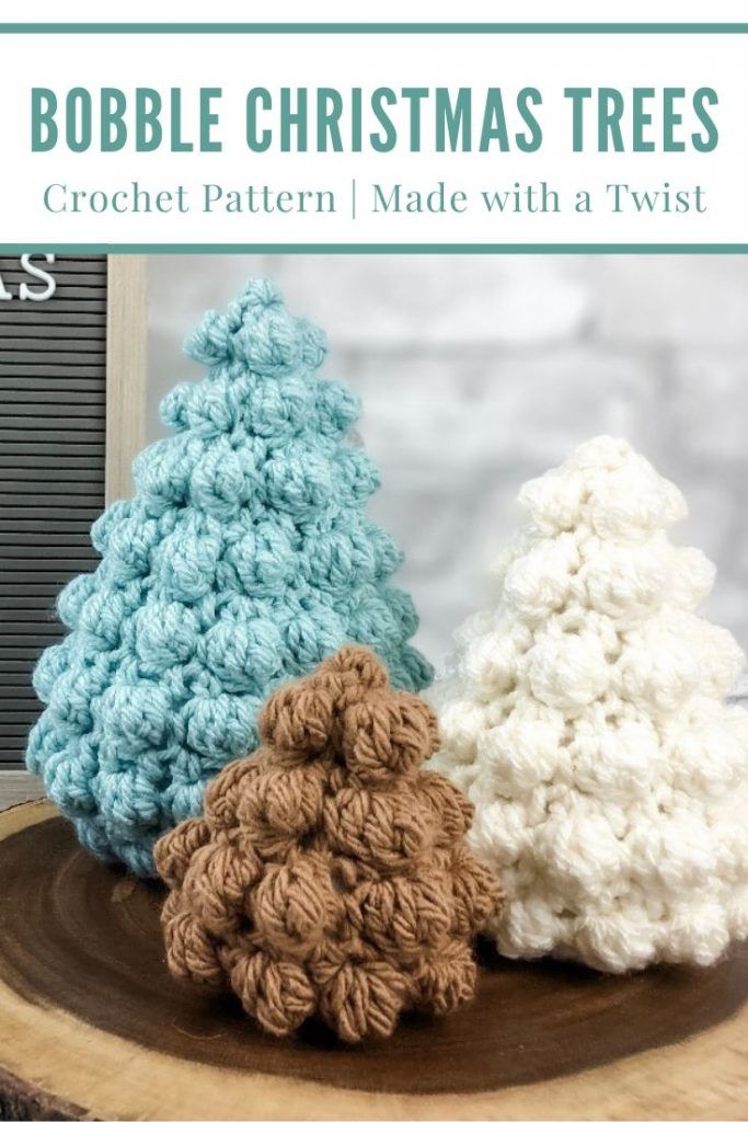 three crocheted christmas trees sitting on top of a tree stump