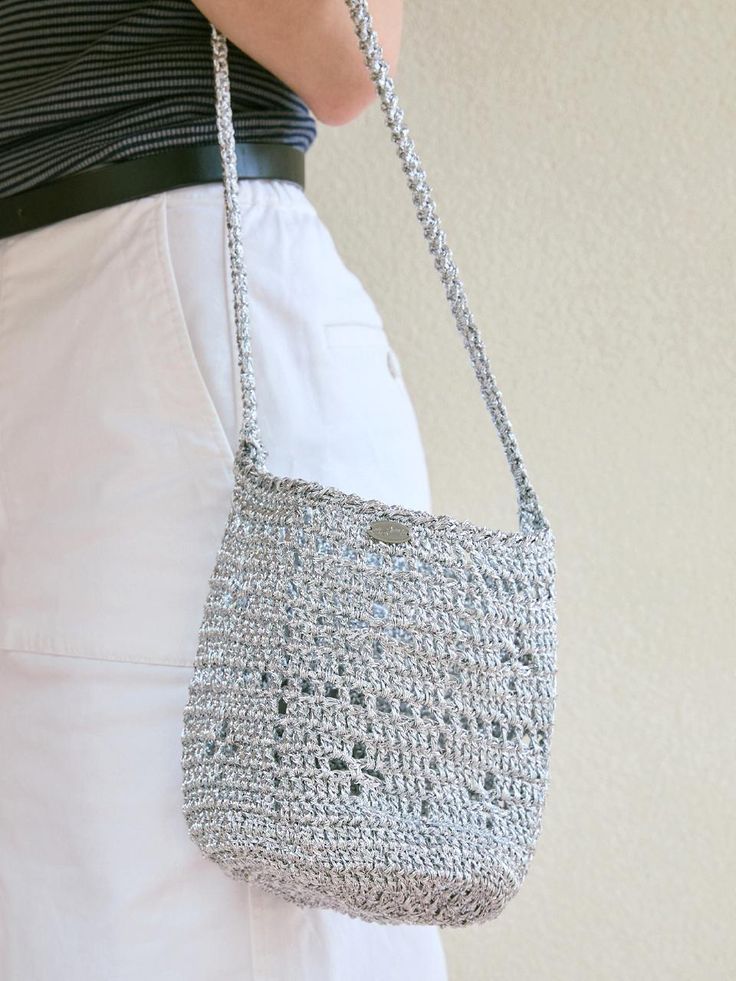 a woman is holding a crocheted purse in her right hand and wearing white pants