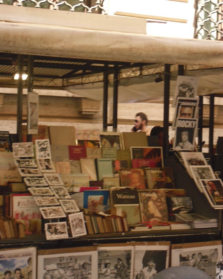 a man standing in front of a book stand with many books on it and people looking at them