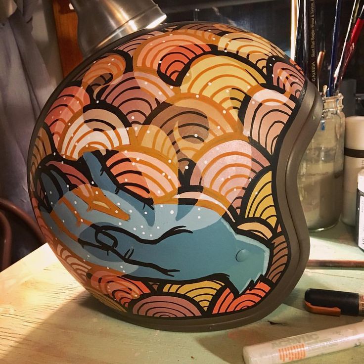 a painted helmet sitting on top of a wooden table next to paintbrushes and markers