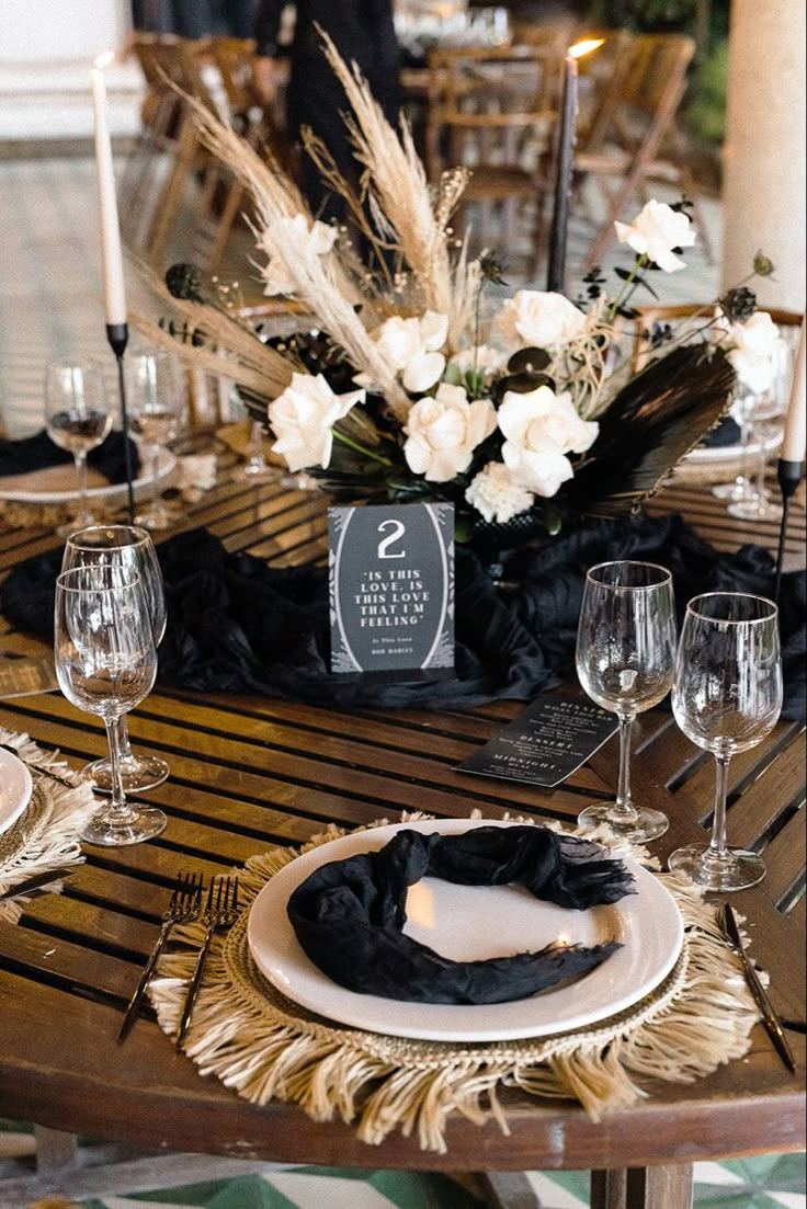 the table is set with white flowers and black napkins, silverware, and wine glasses