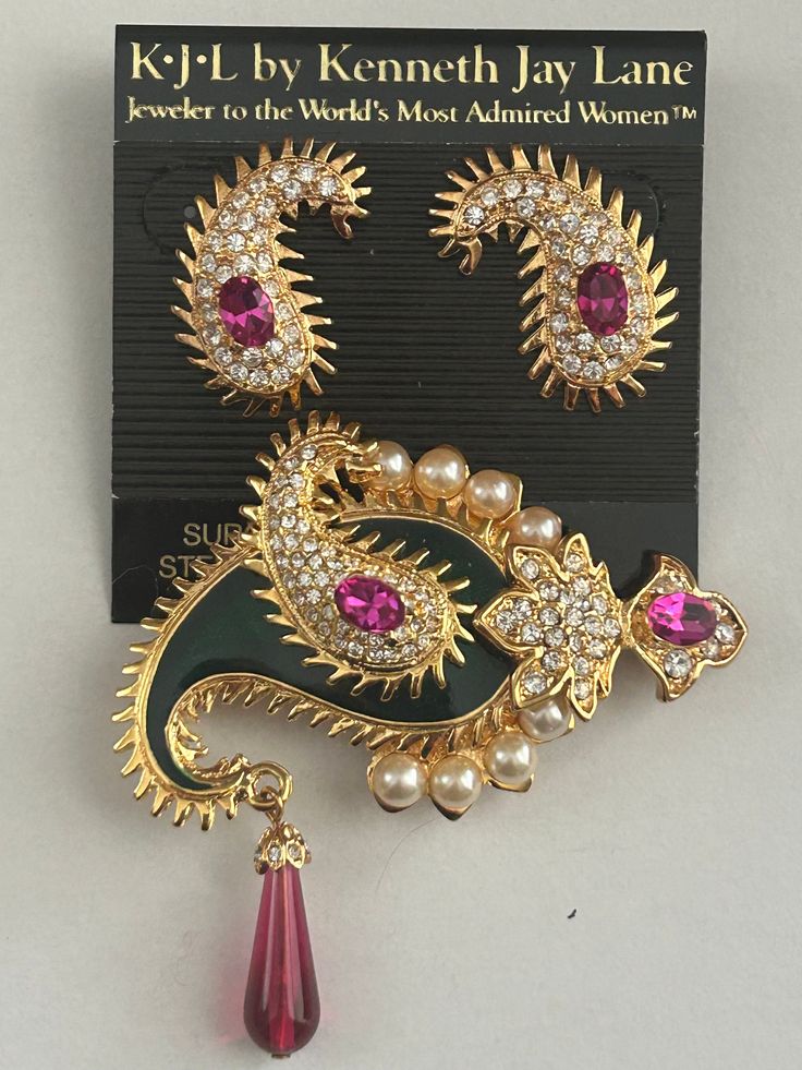 A stunning vintage brooch and pierced earring set by Kenneth Jay Lane.  The beautiful set is from the KJL Maharaja collection, Jewels of India.  The brooch features a gold plated paisley design in a dark green enamel background. It has 8 faux pearls around the outside edge. Pave set clear crystals, snd 2 faux pink sapphires. It is a layered pin and a dark pink teardrop shaped lucite stone dangles off of it.  It is marked on the back: KJL The pin measures approximately 2 1/2 inches long, and 2 1/2 inches wide. The surgical steel post earrings are a gold plated paisley design with clear pave set rhinestones, and a faux pink sapphire in the center. They measure approximately 1 inch long.  This set is brand new in its original red box, cloth bag, and warranty card. It is pristine and in excell Vintage Earrings For Formal Festive Occasions, Festive Vintage Formal Earrings, Traditional Collectible Jewelry Brooch, Traditional Formal Brooch With Intricate Design, Ornate Stone Work Earrings For Gift, Festive Gold Jewelry With Brooch, Ornate Stone Work Earrings As Gift, Wedding Costume Jewelry Brooches With Matching Earrings, Handmade Traditional Brooch For Formal Occasions