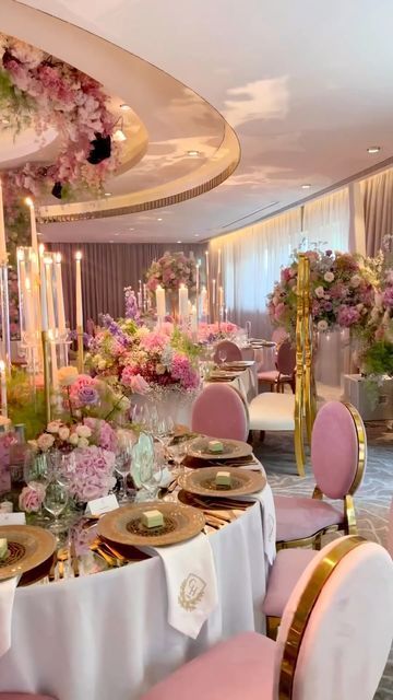 a dining room set up with pink chairs and white table cloths, gold trimmed plates and flowers