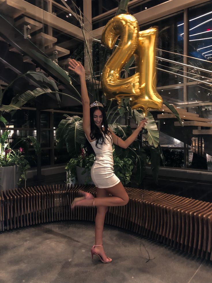 a woman holding up the number twenty two balloons in front of her face and standing on one leg