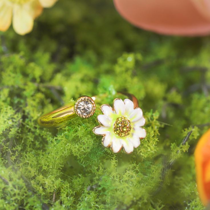 The Daisy Ring, with its open and adjustable design, feels like a delicate bloom resting upon your hand. Each petal is handcrafted in enamel, set upon 18K gold-plated brass, as though plucked straight from a morning garden. A sparkling cubic zirconia sits at the heart of the daisy, catching the light like morning dew. The adjustable band ensures a perfect fit, allowing this graceful flower to adorn any finger, bringing with it a timeless charm and a reminder of nature’s simple beauty. DETAILS Plating: 18K Gold Materials:   18K Gold on Brass, Enamel, Cubic Zirconia Size: Adjustable, 0.47"*0.67"(12mm*17mm) Weight: 3.5 g Gold Enamel Flower Ring For Anniversary, Adjustable Gold Flower Ring, Yellow Gold Enamel Flower Ring Gift, Gold Flower-shaped Enamel Ring, Gold Enamel Flower Ring, Dainty Flower-shaped Enamel Jewelry, Adjustable Flower Enamel Ring As Gift, Dainty Adjustable Enamel Jewelry, Flower Shaped Enamel Ring As A Gift