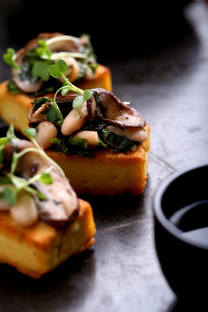 three pieces of bread with mushrooms and greens on top, next to a black cup