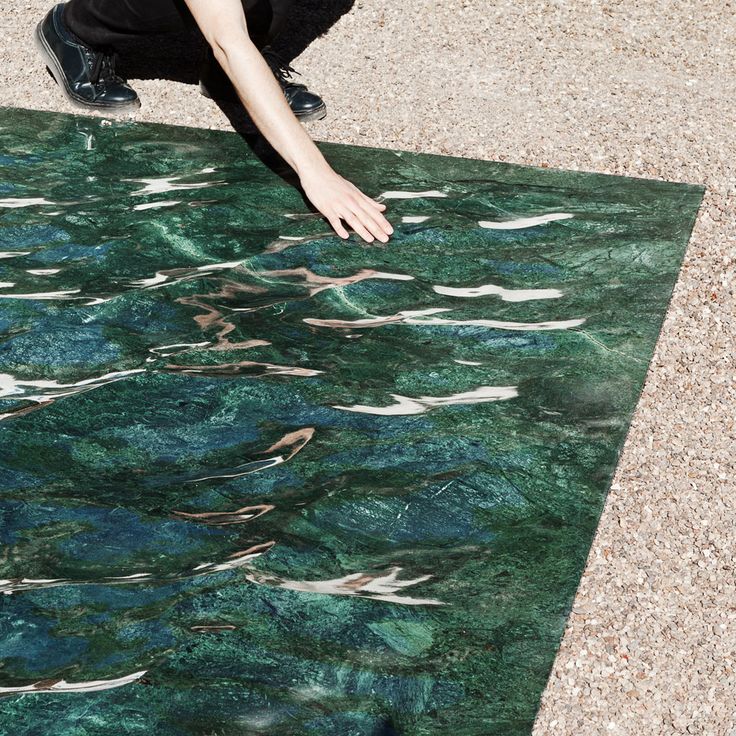 a man kneeling down on top of a rug next to a body of blue water