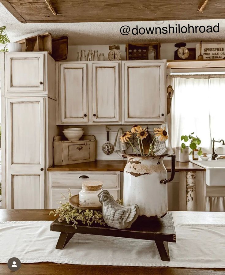 an old fashioned kitchen with white cabinets and flowers in the pot on the counter top