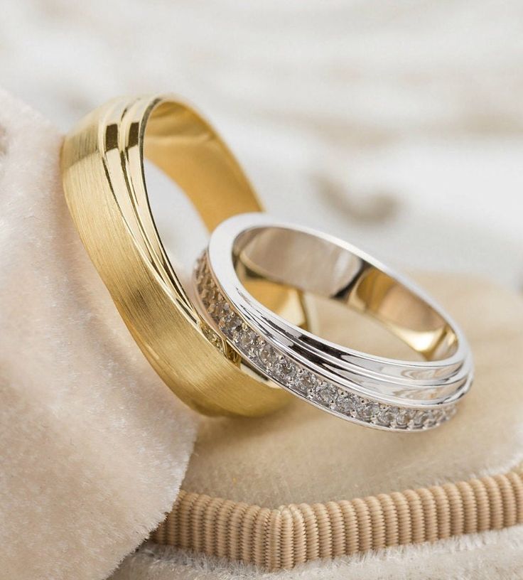 two gold wedding rings sitting on top of a white cloth next to a ring holder