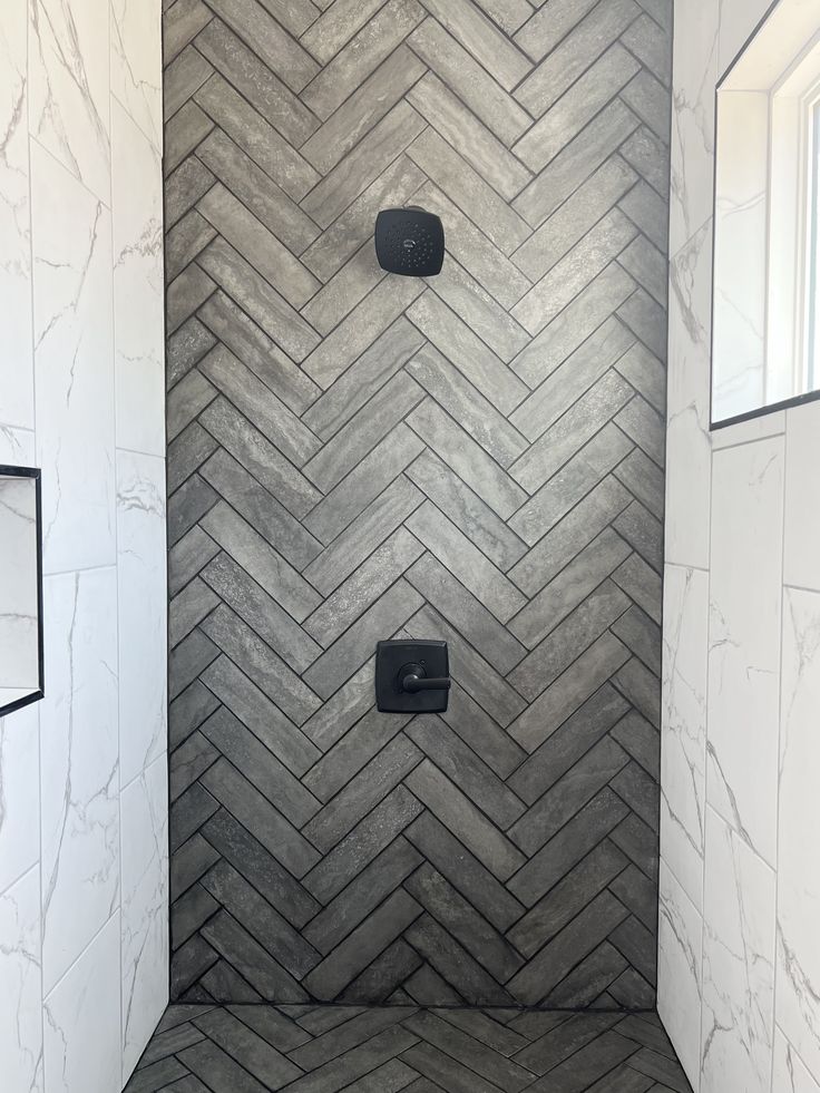 a walk in shower sitting next to a white tiled wall and floor covered in gray herringbone tile