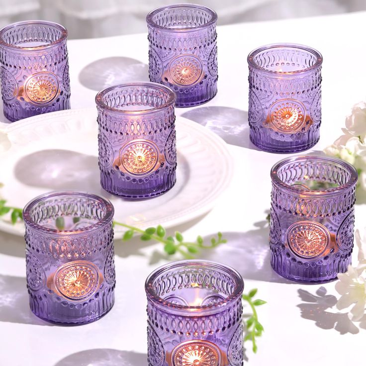 six purple glass candles sitting on top of a table next to white plates and flowers