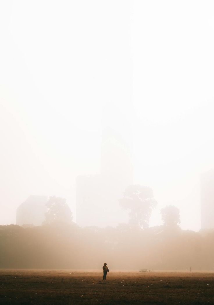 a person is flying a kite in the foggy field with buildings behind them on a sunny day