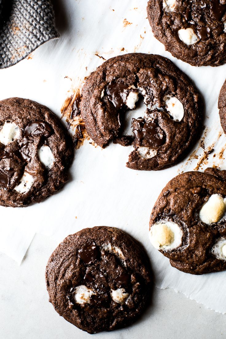 chocolate cookies with marshmallows are arranged on a piece of parchmented paper