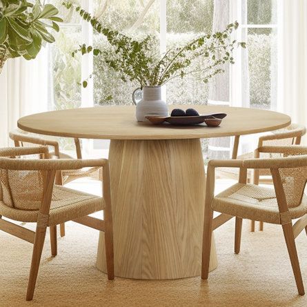 a wooden table with chairs around it in front of a window and potted plant