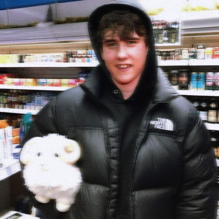 a young man in a black jacket holding a stuffed animal and wearing a hoodie