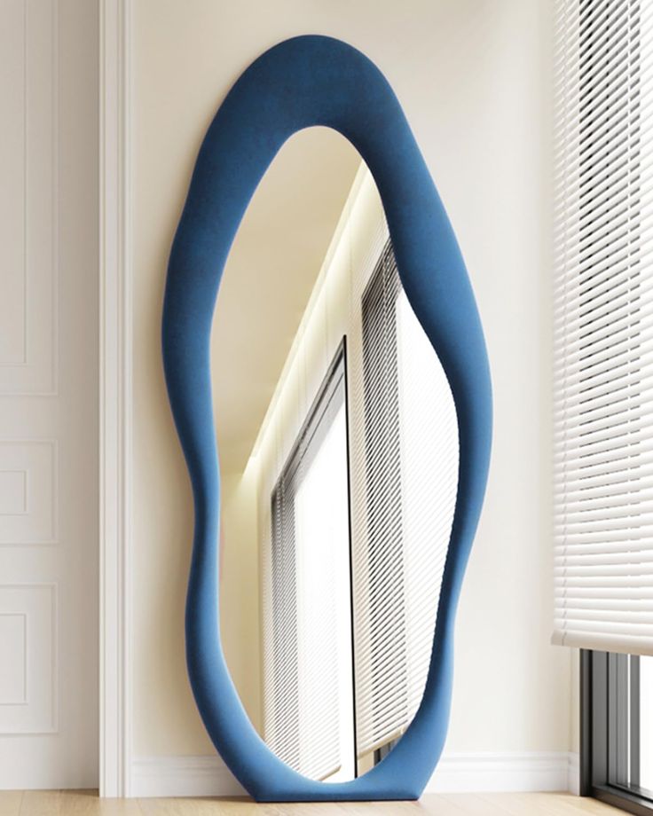 a blue oval mirror sitting on the side of a white wall next to a window