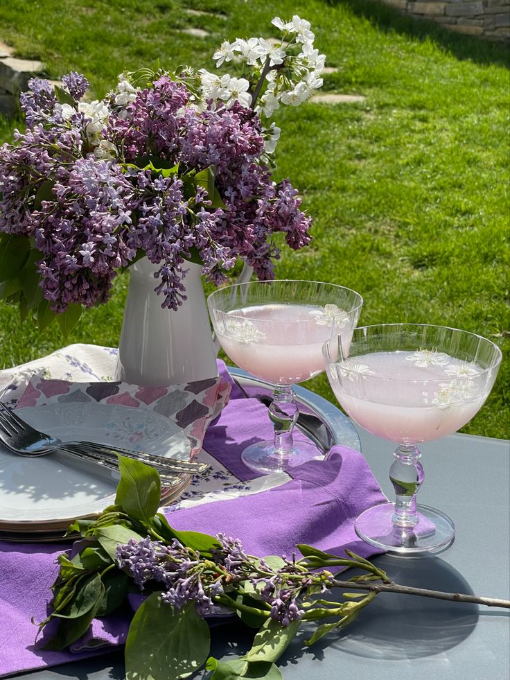 the table is set with two glasses and flowers in vases on top of it