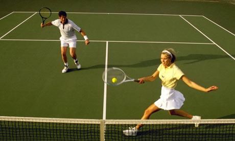 two people playing tennis on a court with one hitting the ball and the other holding the racket