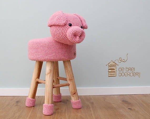 a pink knitted pig sitting on top of a wooden stool next to a wall