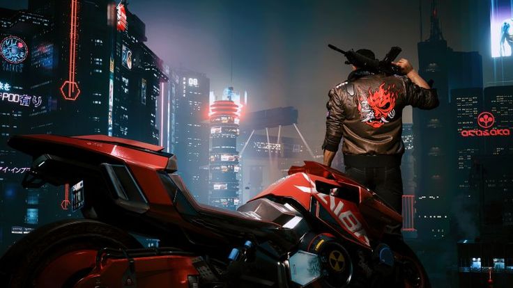 a man standing next to a red motorcycle in the middle of a city at night