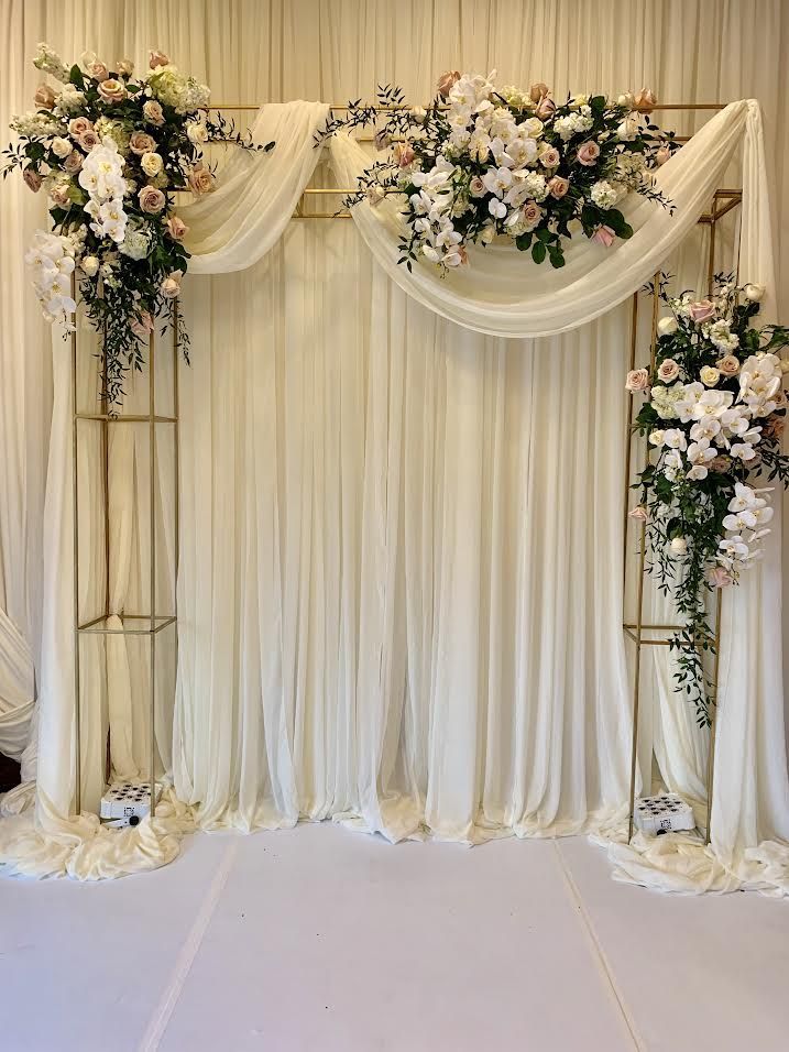 an image of a wedding ceremony setting with flowers on the wall and white drapes