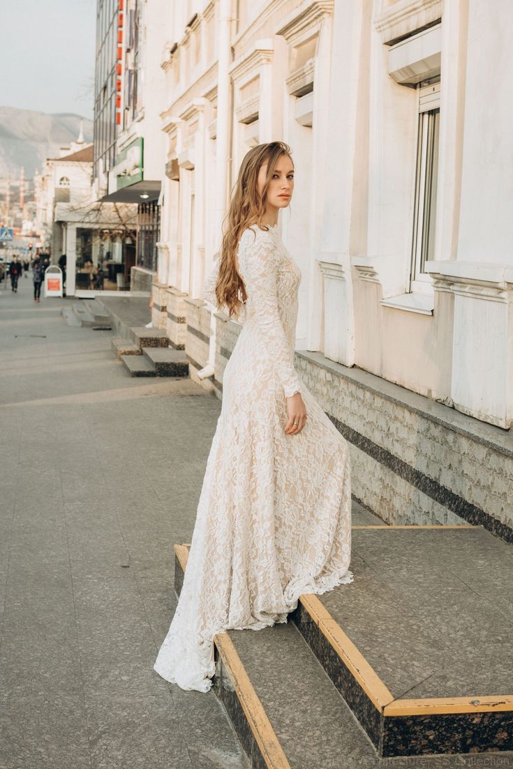 a woman in a long white dress is standing on some steps and looking off into the distance