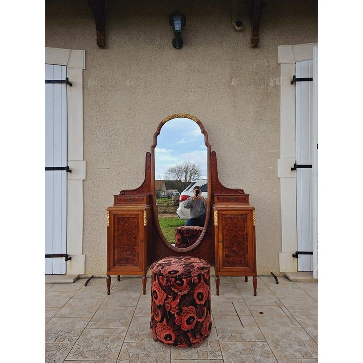 a mirror sitting on top of a wooden dresser next to a table with a stool