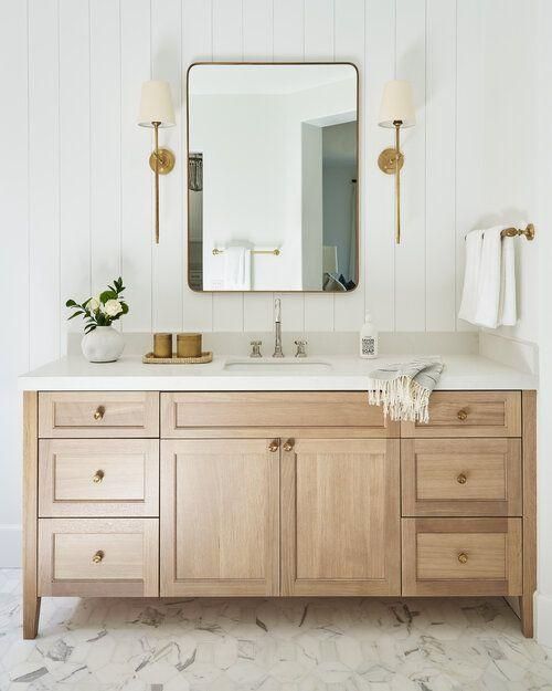 a white bathroom with wooden cabinets and marble counter tops, along with a large mirror on the wall