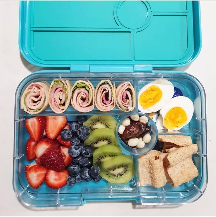 an open lunch box filled with fruit, crackers and eggs