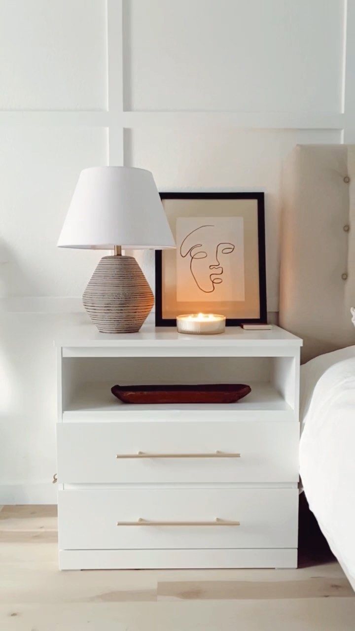 a night stand with a lamp on it next to a bed