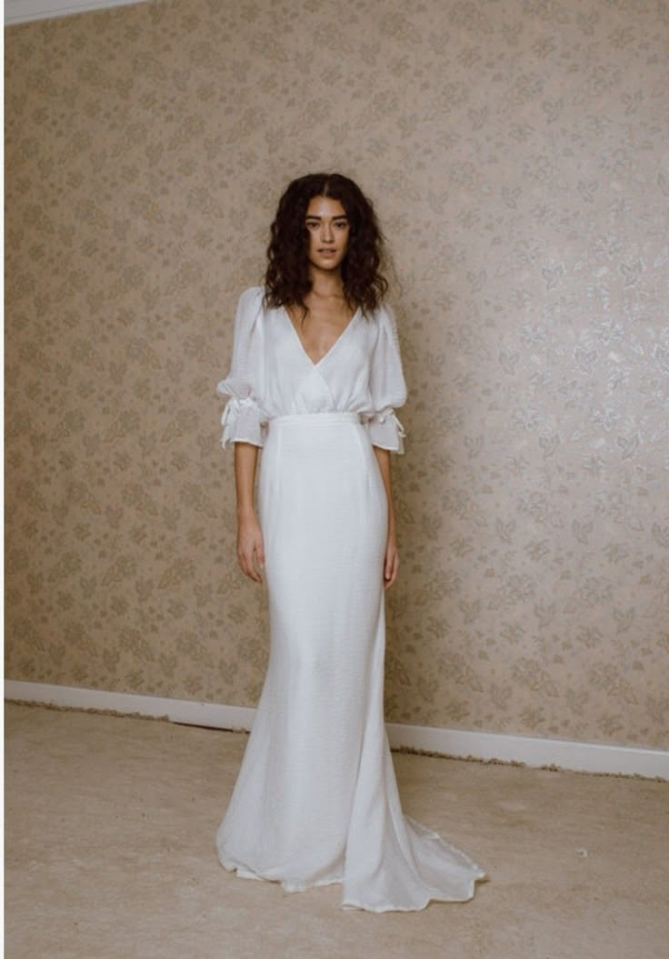 a woman standing in front of a wall wearing a white dress