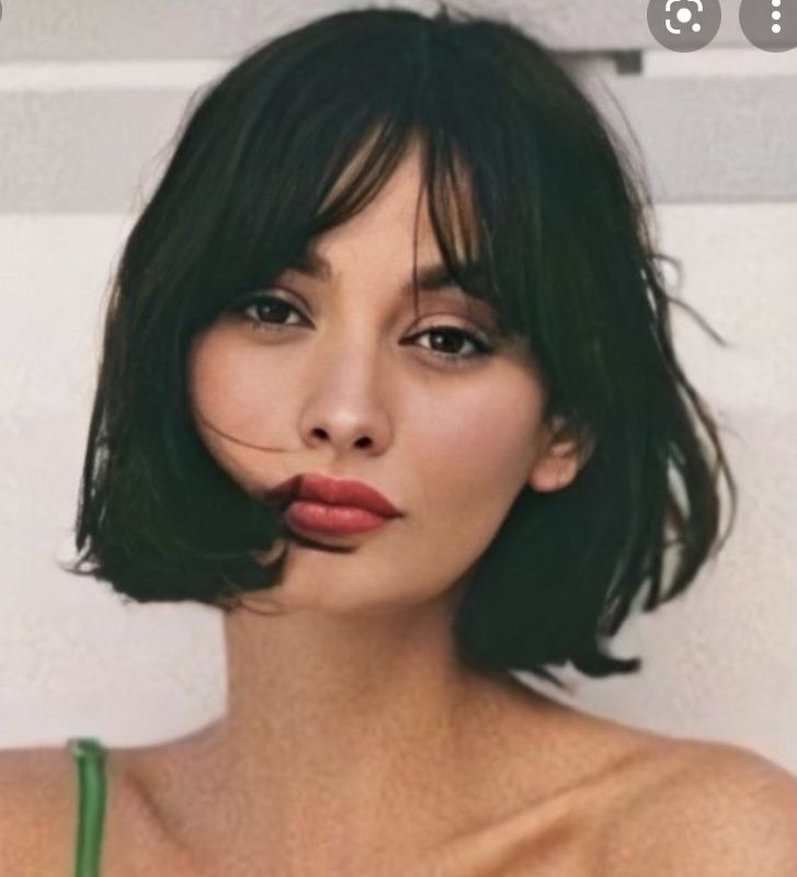 a woman with short black hair wearing a green bra and lipstick on her lips, in front of a brick wall