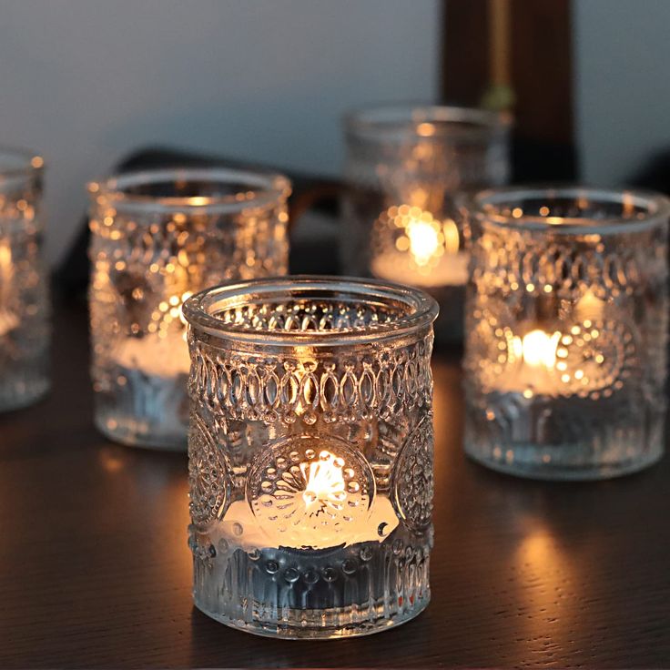 lit candles are sitting on a table in glass jars with lace designs and small ones