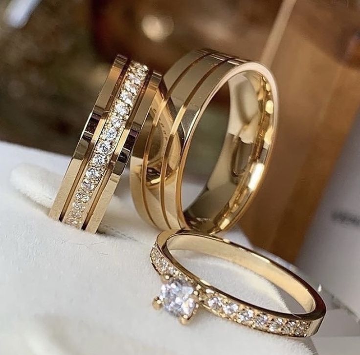 two gold wedding rings with diamonds on them sitting on a white cloth in front of a mirror