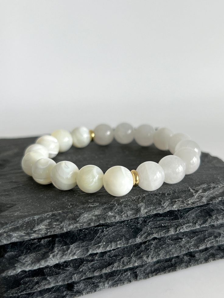 💎 MATERIAL DETAILS ○ 10mm Mother of Pearl Shell → soothing, stimulates adaptability, intuition, and imagination  ○ 10mm White Jade → abundance, prosperity, detox, calmness, and love ○ 6mm 18k gold plated spacers ○ High quality, resistant, and flexible elastic cord (double-corded) 💯 QUALITY & CRAFTSMANSHIP ○ Materials are handpicked, inspected, and handled with the utmost quality and care ○ Double-corded with high quality elastic cord - this means our bracelets have 2x the durability of other s White Spiritual Pearl Bracelet With Gemstone Beads, Spiritual White Pearl Bracelet With Gemstone Beads, White Pearl Bracelet With Gemstone Beads For Spiritual Wear, White Beaded Gemstone Bracelets For Everyday, Everyday White Beaded Gemstone Bracelets, Spiritual White Pearl Bracelet With 8mm Beads, Spiritual Style White Pearl Bracelet With 8mm Beads, White Gemstone Beads Bracelet As Gift, Minimalist White Gemstone Bracelet