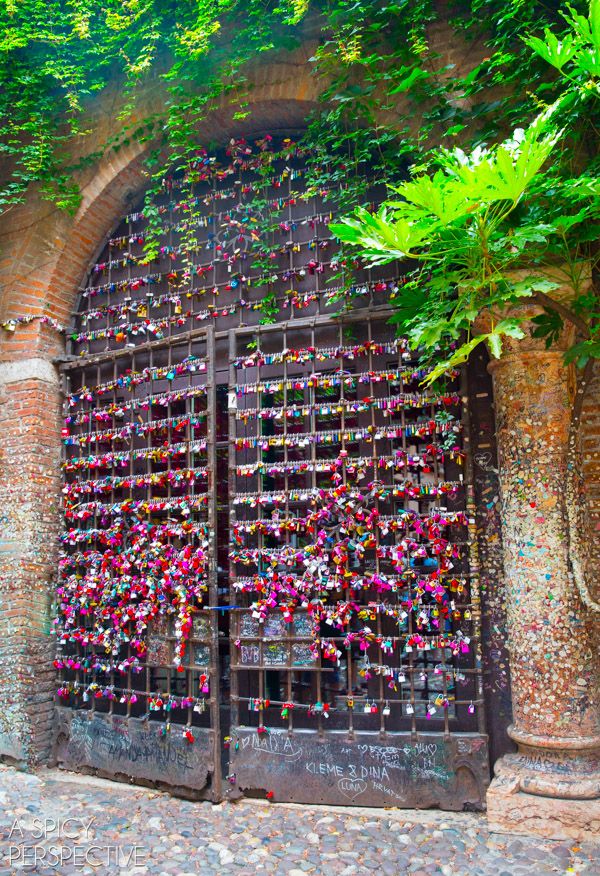 an iron gate covered in lots of padlocks next to a tree and brick wall