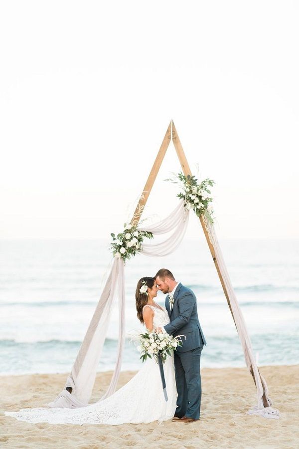 a bride and groom kissing on the beach in front of an arch decorated with flowers