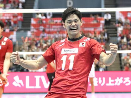 two men in red uniforms playing volleyball on a court with people watching from the stands