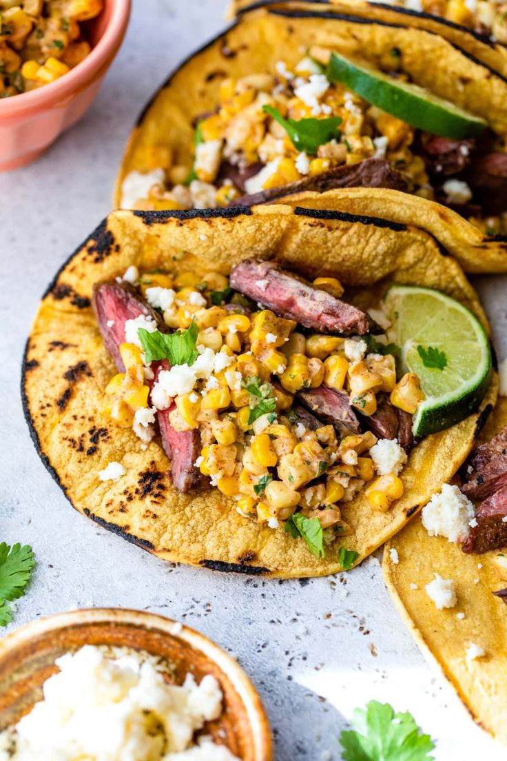 corn and steak tacos with lime wedges on the side next to bowls of salsa