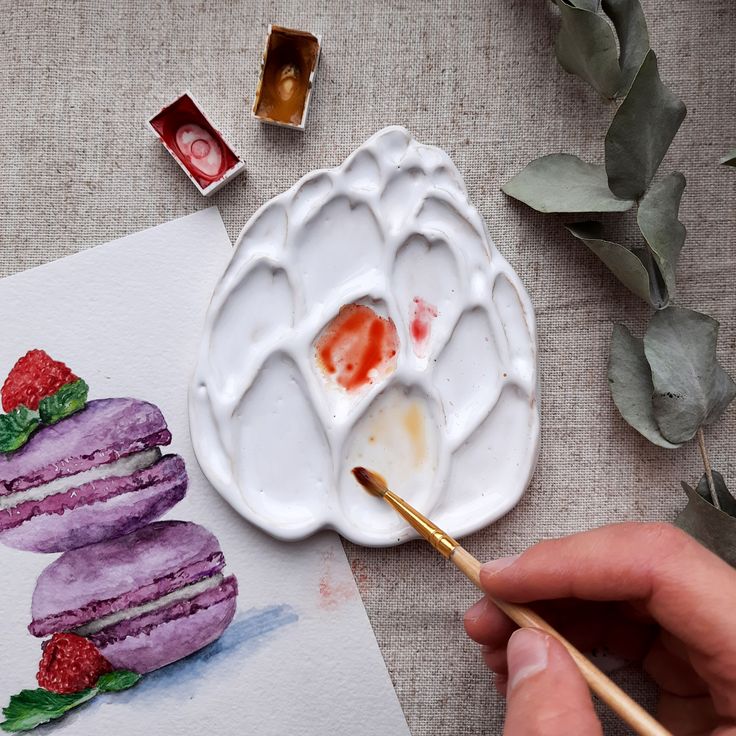 a person is painting some food on a plate with watercolors and paintbrushes