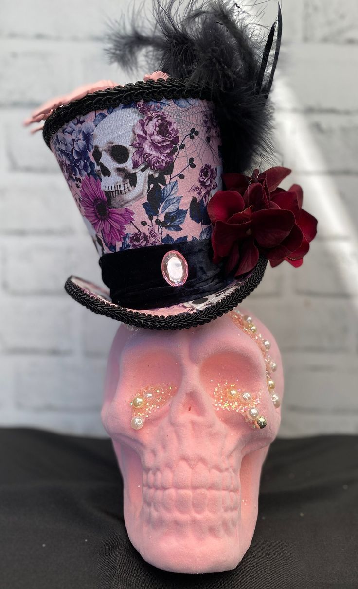 a pink skull wearing a top hat with black feathers and flowers on it's head