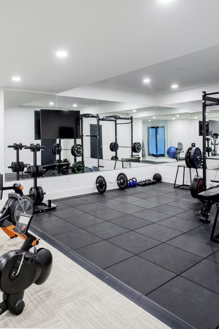 an empty gym room with exercise equipment and mirrors on the wall, along with black tile flooring