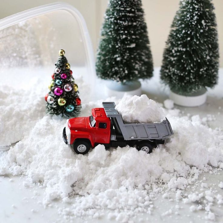 a toy truck is parked in the snow next to small christmas trees and other decorations