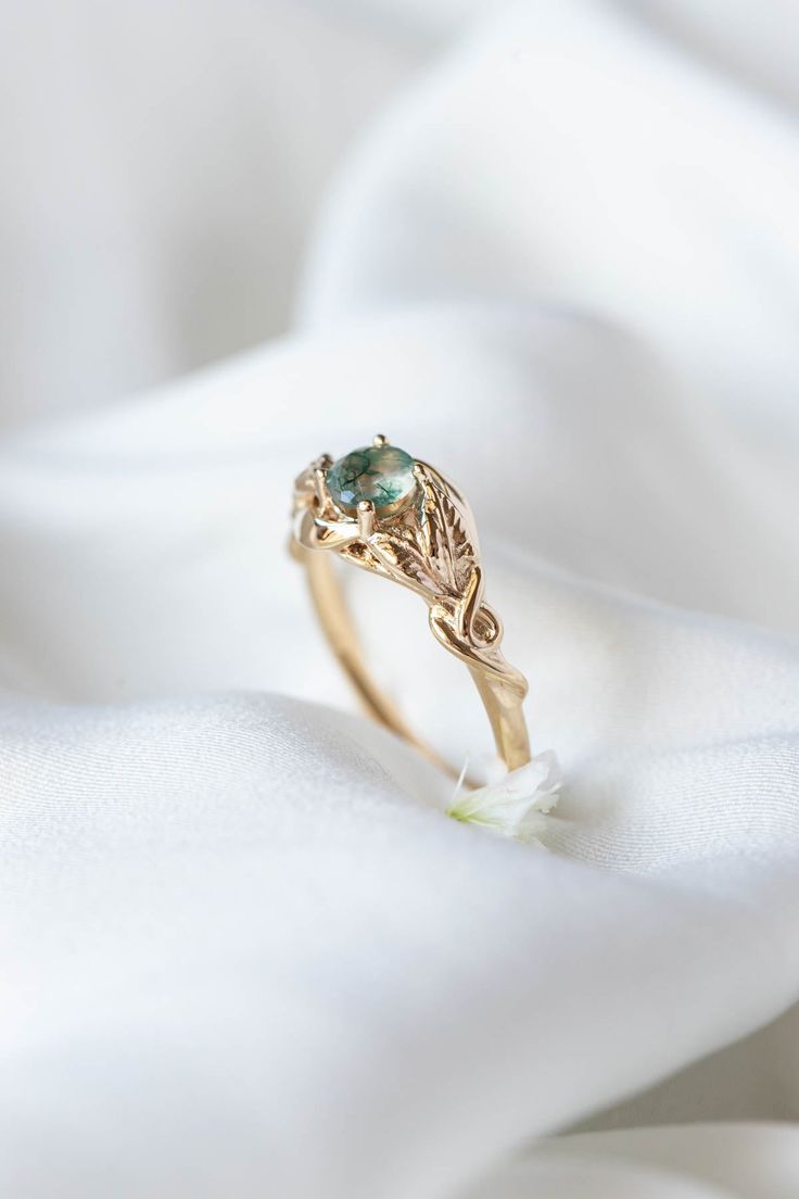 a close up view of a gold ring with a green stone in the center on a white cloth