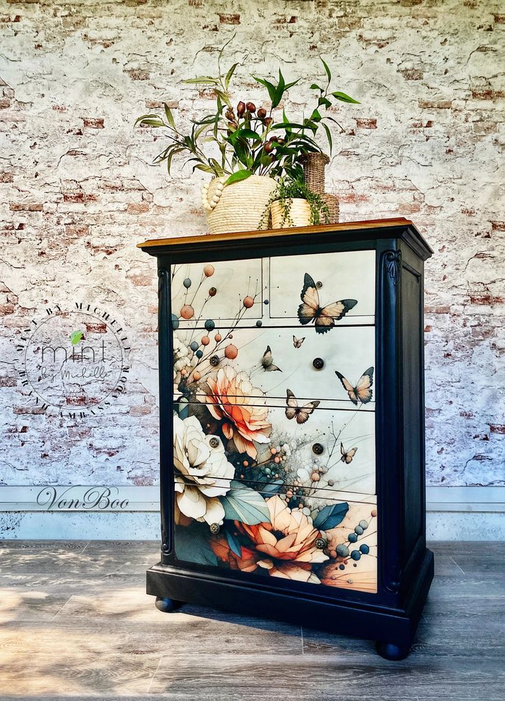 a painted cabinet with flowers and butterflies on the front, against a white brick wall