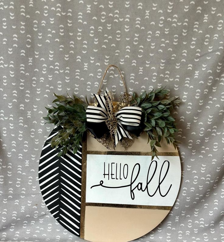 a sign that says hello fall hanging from the side of a wall with greenery on it