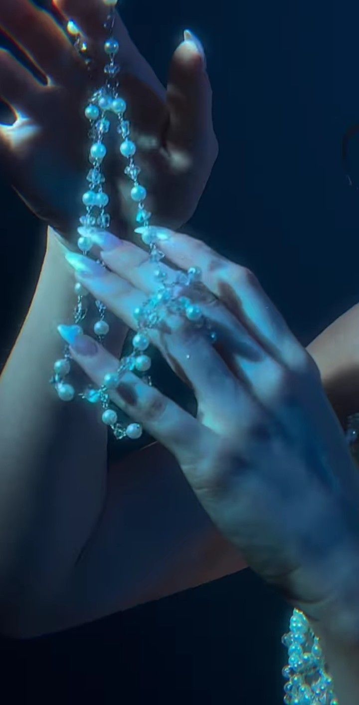 a woman holding beads in her hands with blue light shining on her body behind her