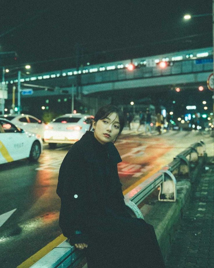 a person sitting on a bench in front of a street with cars driving by at night