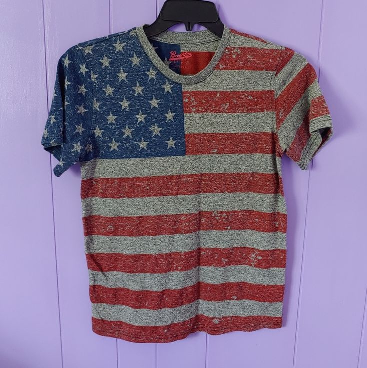 an american flag t - shirt hanging on a hanger in front of a purple wall