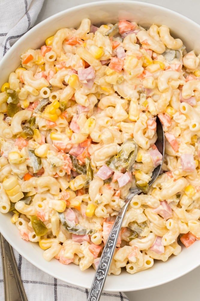 a white bowl filled with macaroni salad next to a silver spoon and fork